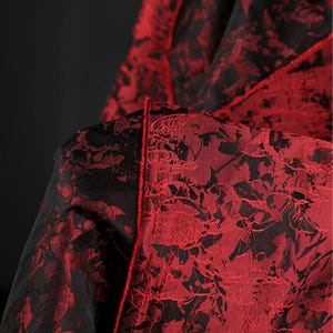 K&ouml;nnte beinhalten: Nahaufnahme eines Stoffes mit floralem Muster. Der Stoff ist tiefrot mit schwarzen Akzenten, was einen auff&auml;lligen Kontrast erzeugt. Das florale Design ist detailliert und komplex, mit einem strukturierten Aussehen. Die Kanten sind mit einem roten Besatz versehen.
