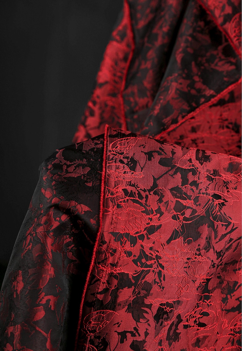 K&ouml;nnte beinhalten: Nahaufnahme eines Stoffes mit floralem Muster. Der Stoff ist tiefrot mit schwarzen Akzenten, was einen auff&auml;lligen Kontrast erzeugt. Das florale Design ist detailliert und komplex, mit einem strukturierten Aussehen. Die Kanten sind mit einem roten Besatz versehen.