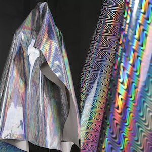May include: Holographic fabric, draped and rolled. The draped fabric displays a spectrum of colours and has a perforated texture. The rolled fabric has a wavy, black and white pattern with rainbow highlights, creating an iridescent effect.