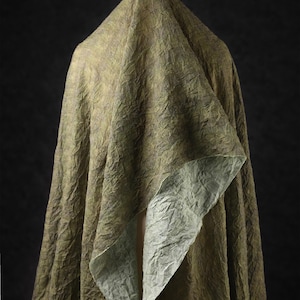 May include: A draped fabric with a textured, crinkled appearance. The outer layer is a muted olive green, while the underside reveals a lighter, silvery-green hue. The fabric is arranged to create folds and shadows against a dark background.
