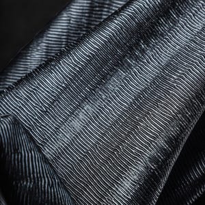May include: Close-up of a textured fabric with a pattern of parallel, slightly curved lines. The fabric appears to be a dark gray or black color, with subtle highlights creating a sense of depth and dimension. The material is folded.