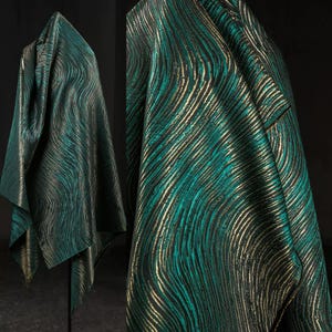 May include: A teal, black, and gold patterned fabric. The material is draped to display the wavy design. The image highlights the fabric's texture and colour variations. The fabric is likely for clothing or home decor.