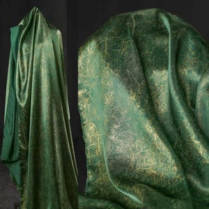 May include: Emerald green fabric with a metallic gold vein-like pattern. The fabric is draped, showcasing its texture and sheen. The material appears to be luxurious, suitable for apparel or home decor.