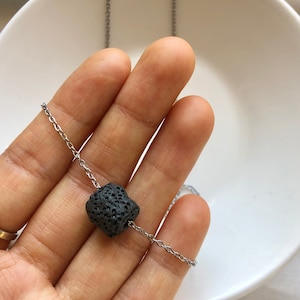 Peut inclure: Un collier en chaîne argent avec un pendentif en pierre de lave noire.