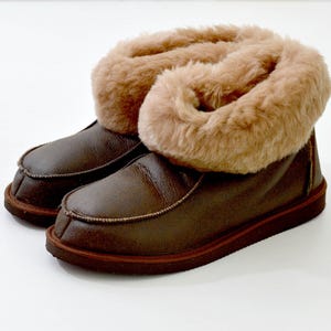 Op de afbeelding: Bruine leren slippers met een voering van imitatiebont. De slippers hebben een omslagmanchet en een bruine rubberen zool.