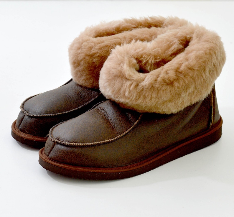 Op de afbeelding: Bruine leren slippers met een voering van imitatiebont. De slippers hebben een omslagmanchet en een bruine rubberen zool.