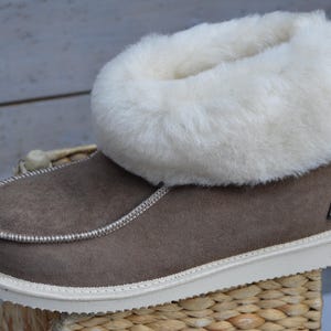 Op de afbeelding: Bruine su&egrave;de pantoffels met een witte nep bontkraag. De pantoffels hebben een witte rubberen zool.