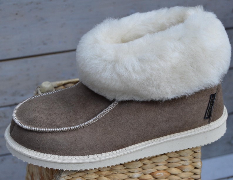 Op de afbeelding: Bruine su&egrave;de pantoffels met een witte nep bontkraag. De pantoffels hebben een witte rubberen zool.