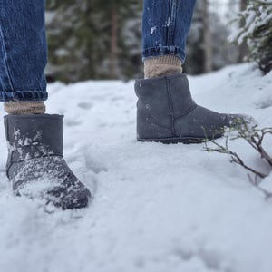 May include: A pair of gray suede boots with a fold-over cuff, worn by a person standing in the snow.