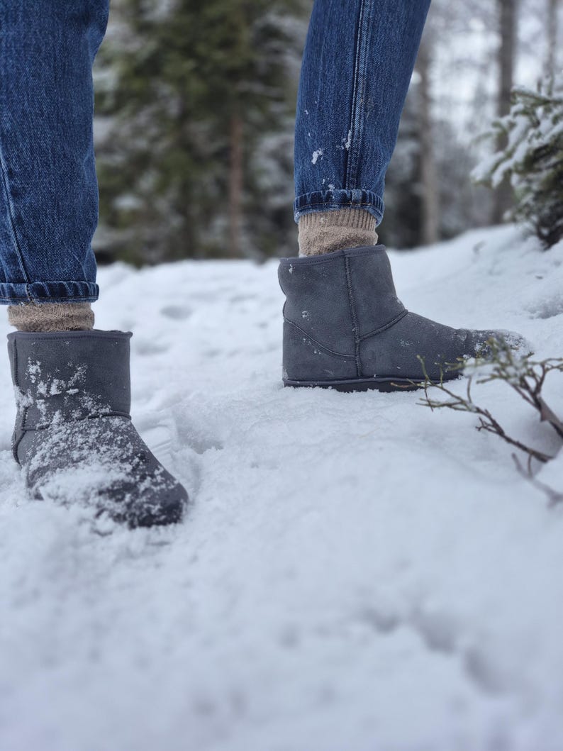 May include: A pair of gray suede boots with a fold-over cuff, worn by a person standing in the snow.
