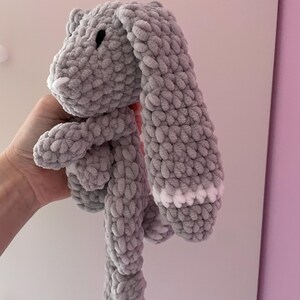 May include: A gray crocheted bunny with white accents on the ears. The bunny is soft and cuddly, perfect for a child's toy.