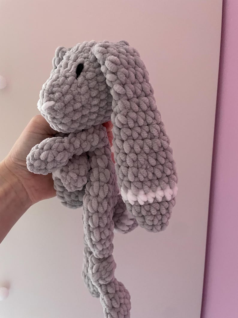 May include: A gray crocheted bunny with white accents on the ears. The bunny is soft and cuddly, perfect for a child's toy.