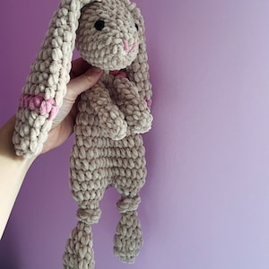 May include: A crocheted plush bunny toy with long ears and pink accents. The bunny is beige and has a soft, fuzzy texture.