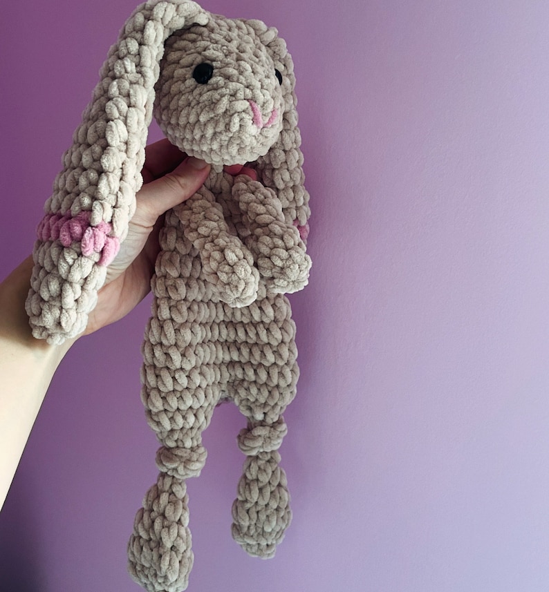 May include: A crocheted plush bunny toy with long ears and pink accents. The bunny is beige and has a soft, fuzzy texture.
