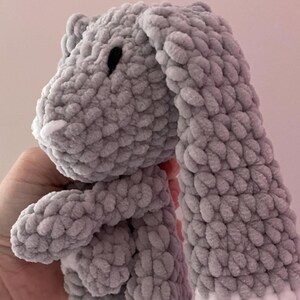 May include: A gray crocheted bunny with white accents on the ears. The bunny is soft and cuddly, perfect for a child's toy.
