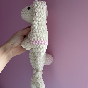 May include: A white crocheted stuffed animal shaped like a dog with pink accents. The dog is standing on its hind legs with its front paws raised.