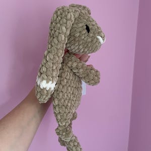 May include: A crocheted brown bunny with white accents on the ears. The bunny is made with a soft, fluffy yarn.