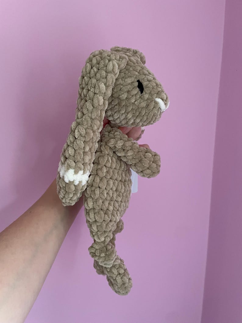 May include: A crocheted brown bunny with white accents on the ears. The bunny is made with a soft, fluffy yarn.