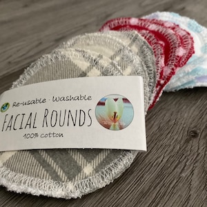 May include: A stack of grey and white reusable facial rounds made of 100% cotton. The rounds are layered on top of each other and have a white stitched edge. The label reads "Re-usable. Washable. FACIAL ROUNDS 100% cotton".