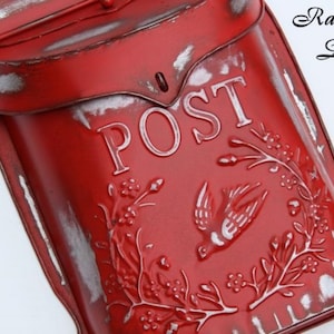 Puede incluir: Buz&oacute;n de metal rojo con un letrero blanco que dice "POST" y un dise&ntilde;o de p&aacute;jaro. El buz&oacute;n tiene un aspecto desgastado y vintage.