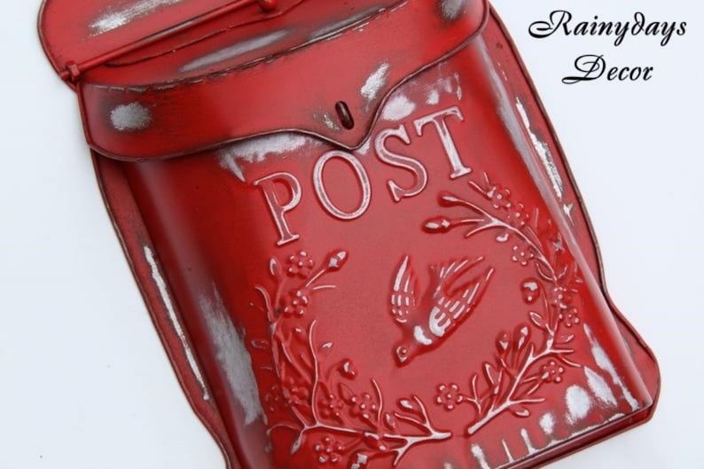Puede incluir: Buz&oacute;n de metal rojo con un letrero blanco que dice "POST" y un dise&ntilde;o de p&aacute;jaro. El buz&oacute;n tiene un aspecto desgastado y vintage.