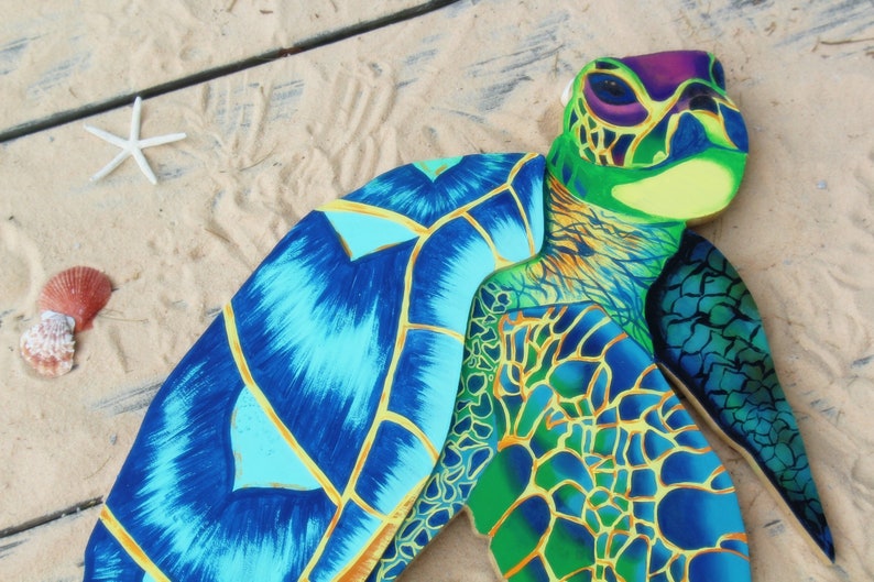 May include: A colorful wooden sea turtle sculpture with blue, green, and yellow paint. The turtle is lying on its back with its shell facing up. The shell is painted with a detailed pattern of scales.