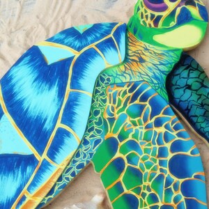 May include: A wooden sea turtle sculpture painted in shades of blue, green, and yellow. The turtle's shell is detailed with a pattern of scales and lines.