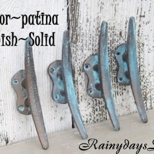May include: Four metal boat cleats with a weathered patina finish, each featuring a central post and two mounting holes at the base. The text Color~patina Finish~Solid and RainydaysDecor is visible on the image, indicating the product details.