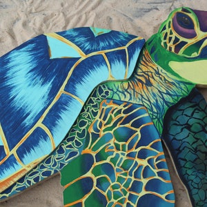 May include: A painted wooden sea turtle sculpture with a blue, green, and yellow shell. The turtle is lying on its back with its head turned to the side.
