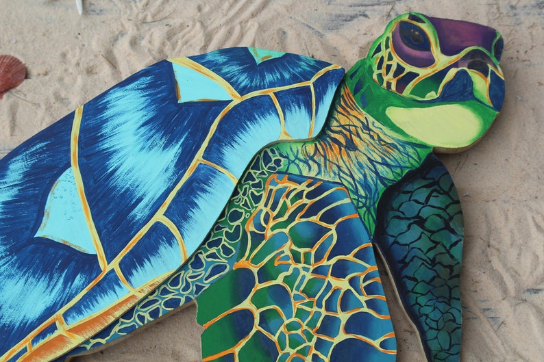 May include: A painted wooden sea turtle sculpture with a blue, green, and yellow shell. The turtle is lying on its back with its head turned to the side.