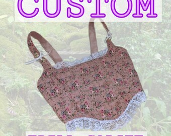 May include: A pink floral print corset with white lace trim and adjustable straps. The corset has a custom design and says "FRILL CORSET" at the bottom.