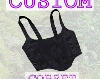 May include: Black custom corset with adjustable straps. The corset has a pointed bottom and is made of a smooth fabric. The text "CUSTOM CORSET" is written in purple below the corset.