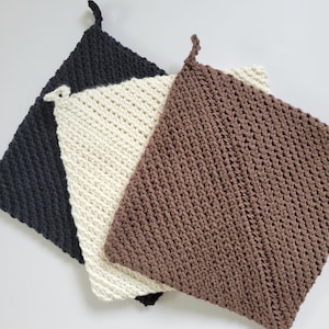 May include: Three crocheted pot holders in black, white, and brown. The pot holders are made with a textured stitch and have a square shape.