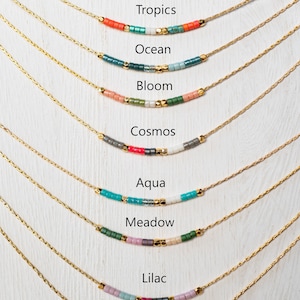 Puede incluir: Nueve collares de oro con cuentas de diferentes colores, cada collar est&aacute; etiquetado con un nombre: Medianoche, Tr&oacute;picos, Oc&eacute;ano, Floraci&oacute;n, Cosmos, Aqua, Prado, Lila, Lirio.