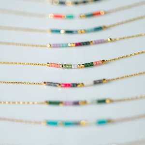 Puede incluir: Un conjunto de delicados collares de cadena dorada con detalles de cuentas de colores. Cada collar presenta una combinaci&oacute;n de colores diferente de cuentas peque&ntilde;as, creando un look &uacute;nico y elegante.
