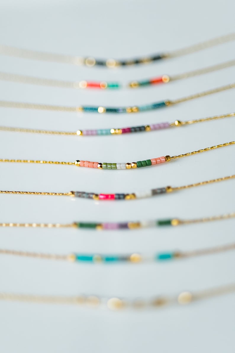 Puede incluir: Un conjunto de delicados collares de cadena dorada con detalles de cuentas de colores. Cada collar presenta una combinaci&oacute;n de colores diferente de cuentas peque&ntilde;as, creando un look &uacute;nico y elegante.