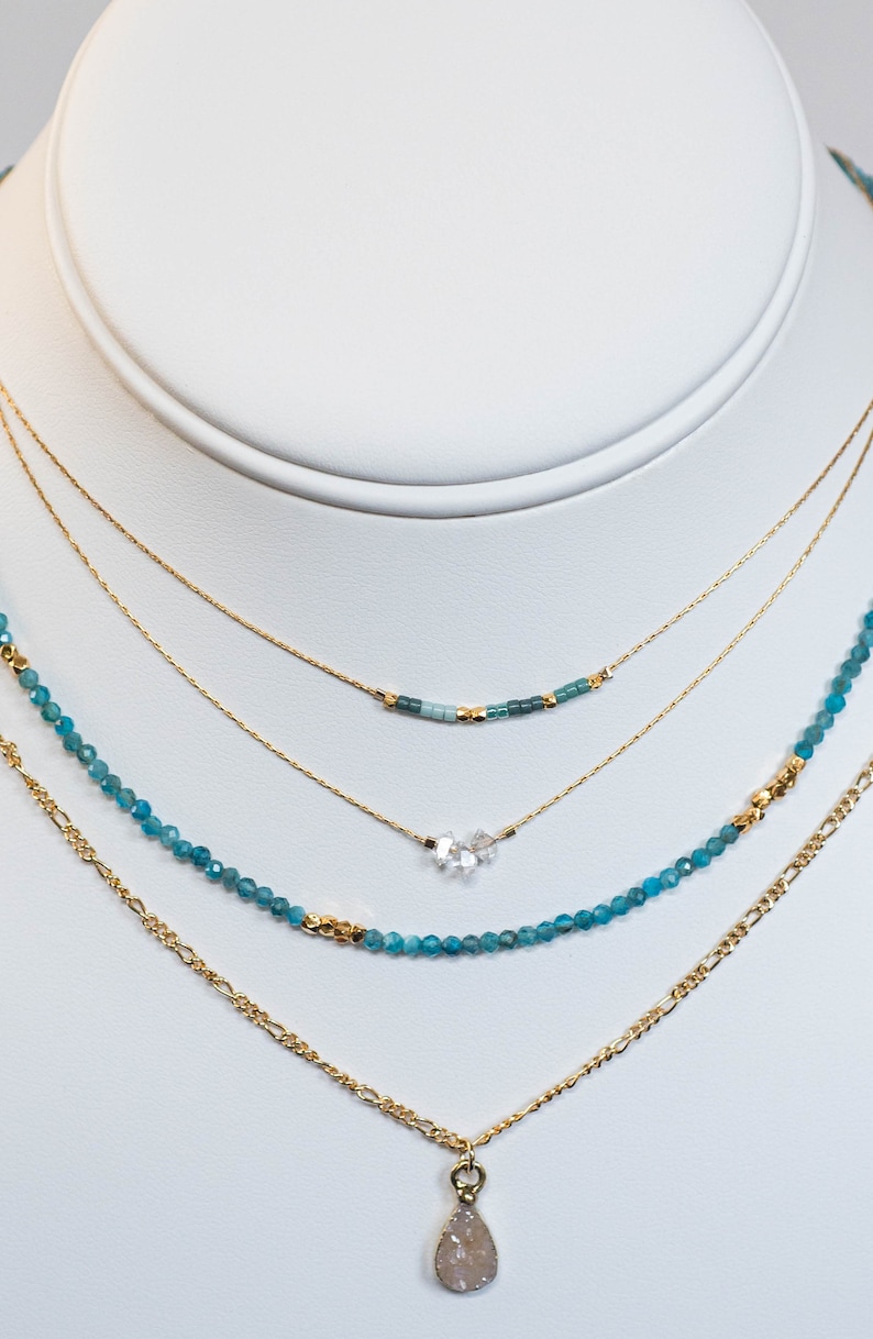 Puede incluir: Un collar de oro de varias capas con un colgante en forma de l&aacute;grima y cuentas de piedras preciosas azules. El colgante est&aacute; hecho de cuarzo transparente.