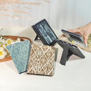May include: An image showing e-reader cases and a tablet with a stand. Two cases have patterned designs in blue and brown. The tablet is propped up with a stand. A hand is holding a clear tablet case with a yellow lightning bolt.