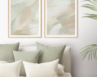 Puede incluir: Dos impresiones artísticas enmarcadas con tonos neutros de beige, blanco y verde. La obra de arte se exhibe sobre una cama con almohadas verdes y blancas y una manta verde. También se ven una planta en maceta y libros.