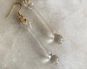 Könnte beinhalten: Ein Paar durchsichtige Glas-Tropfen-Ohrringe mit goldenen Haken.