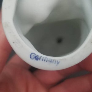 May include: White porcelain figurine with a blue "Germany" mark on the bottom. The figurine has a small hole in the bottom.