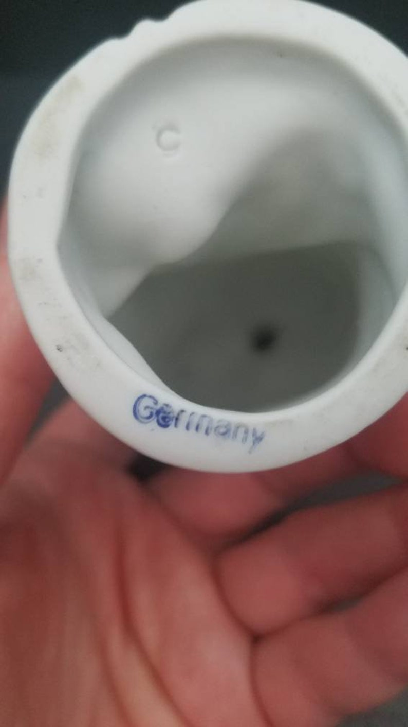 May include: White porcelain figurine with a blue "Germany" mark on the bottom. The figurine has a small hole in the bottom.