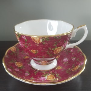 May include: A red teacup and saucer set with a floral pattern. The cup and saucer are decorated with a gold trim.