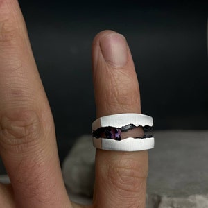 May include: A silver ring with a jagged, broken design. The ring has a purple gemstone set in the center of the break.