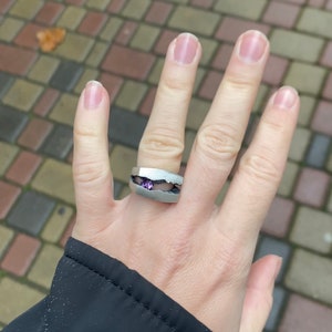 May include: A silver ring with a purple gemstone set in a unique, broken design.