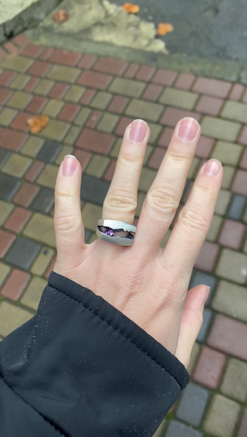 May include: A silver ring with a purple gemstone set in a unique, broken design.