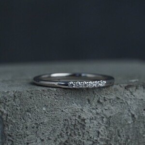 May include: A thin silver band with a row of small diamonds set along the top.