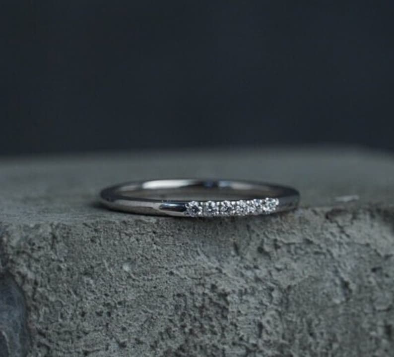May include: A thin silver band with a row of small diamonds set along the top.