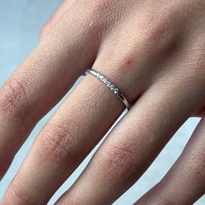 May include: A delicate silver ring with a row of small, clear gemstones set in a thin band.