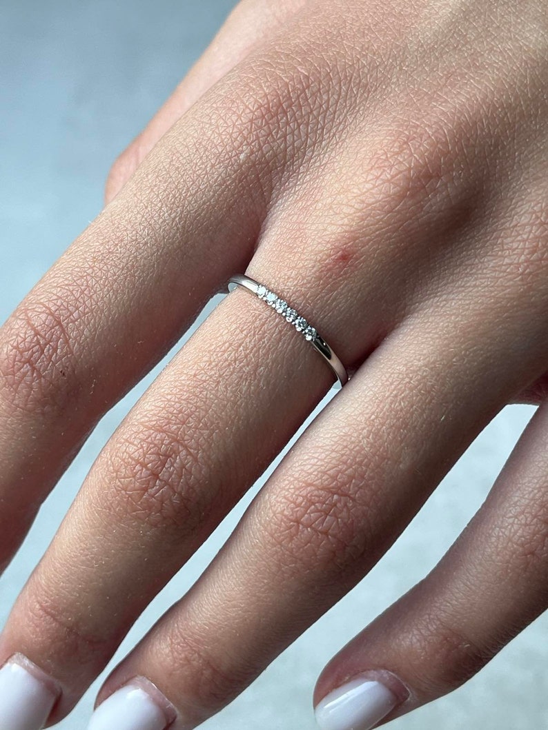 May include: A delicate silver ring with a row of small, clear gemstones set in a thin band.